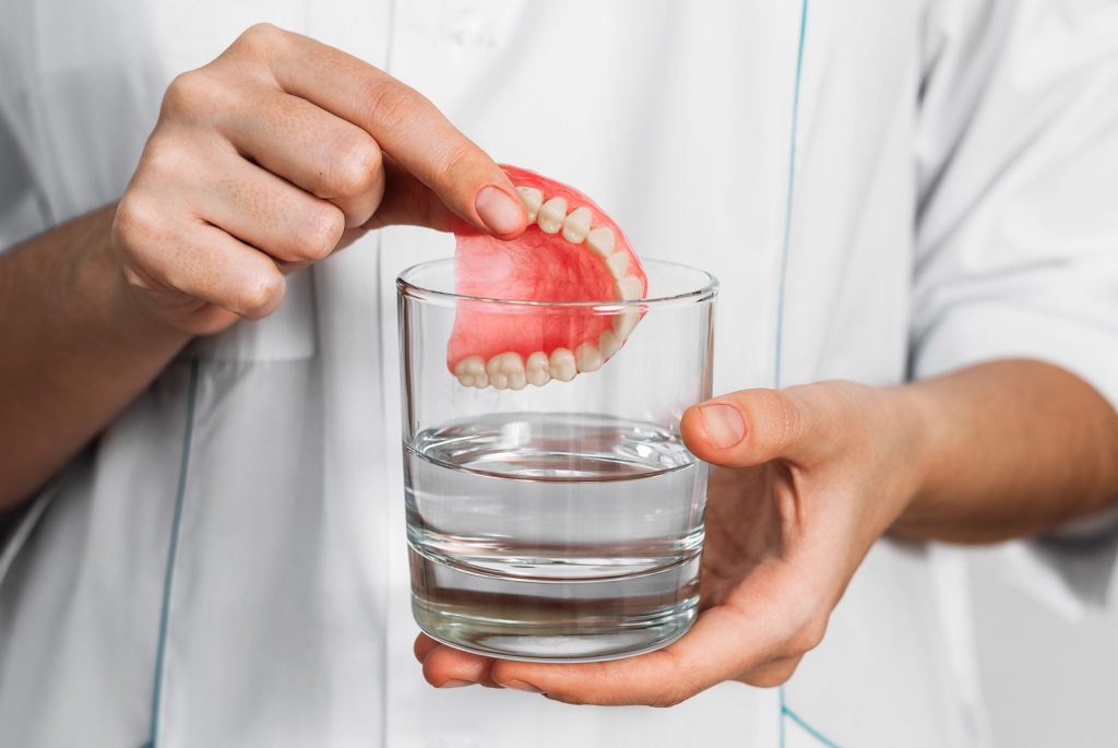 Manos que introducen una dentadura postiza completa removible en un vaso de agua