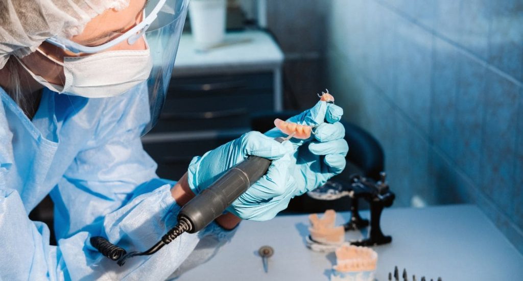 Protésico dental repasando con micromotor una prótesis parcial removible con ganchos